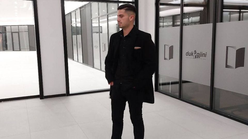 Bright, modern office or showroom corridor with white tile floors and black-framed glass walls and doors. Frosted glass panels display a logo and text, and large windows open to an interior courtyard with additional glass partitions.